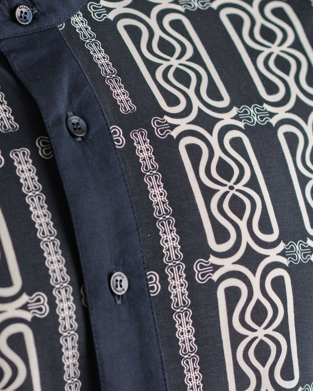 Close view of the RUENCE Ivory raindrop monogram on the Mousson Shirt.